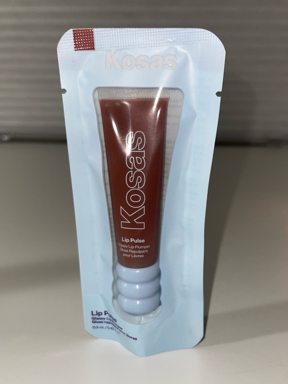Kosas Glossy Lip Pulse Plumper – Deep Brown Tube with Pale Blue Accent